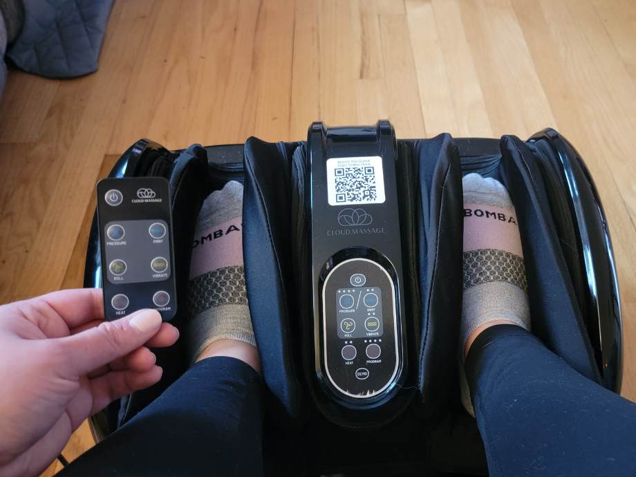 Looking down at feet in the Cloud Massage Shiatsu Foot Massager with remote in hand.