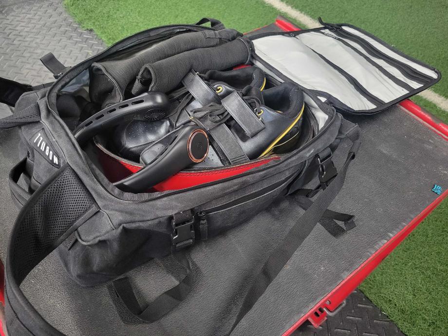 A NOBULL Waxed Canvas Duffleback that's been packed to the brim with gym equipment.