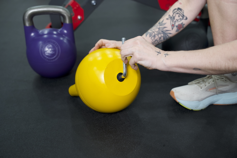 A woman adjusts the Bells of Steel Adjustable Kettlebell using an allen wrench