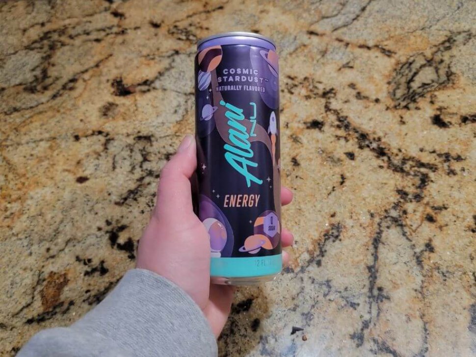 A hand holds out a can of Alani Nu.