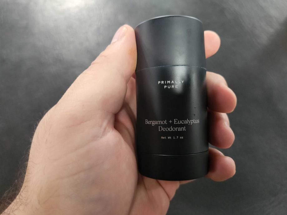 A hand holds a stick of Primally Pure Natural Deodorant.
