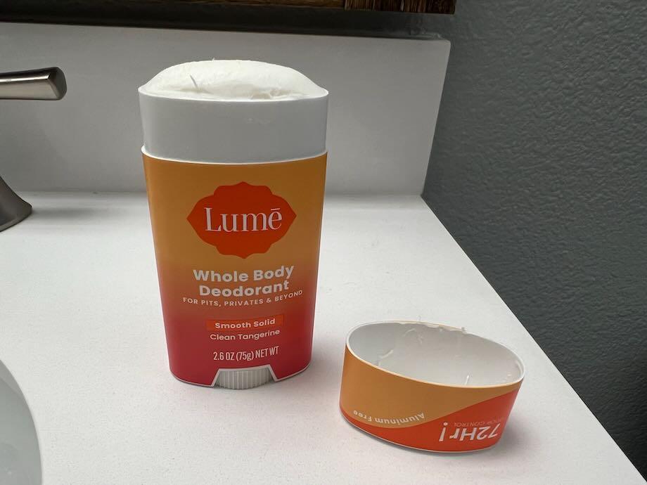 An opened stick of Lume Deodorant setting on a bathroom counter, with the lid resting face-up nearby.