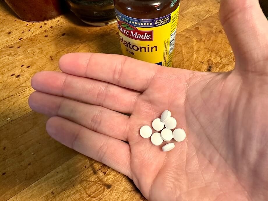 A hand holds some Nature Made Melatonin tablets.