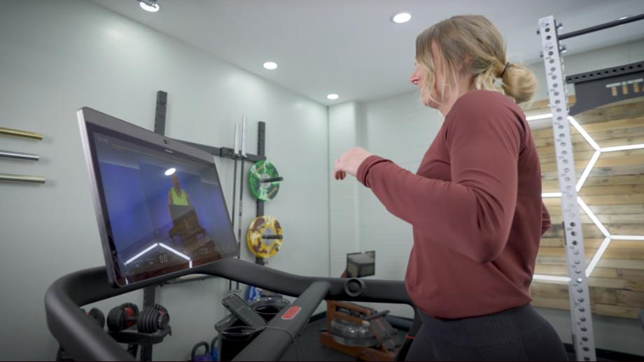A woman runs on the Peloton Tread while looking at the HD touchscreen