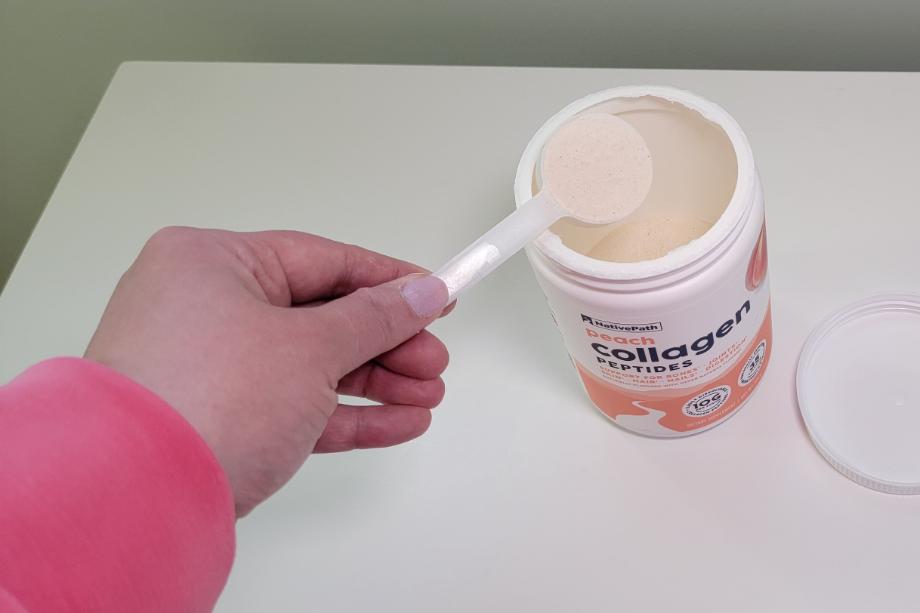 A hand takes a scoop of NativePath Collagen out of the container