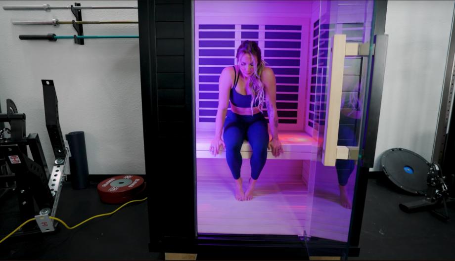 A woman sits in the Sunlighten Amplify II Sauna with chromotherapy lighting on