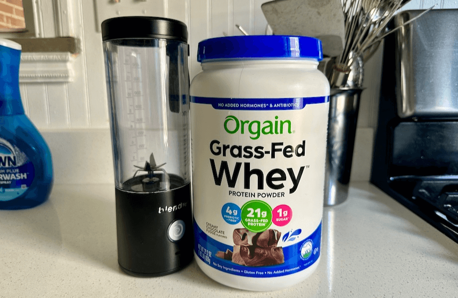 A container of Orgain Grass-Fed Whey Protein next to a portable blender