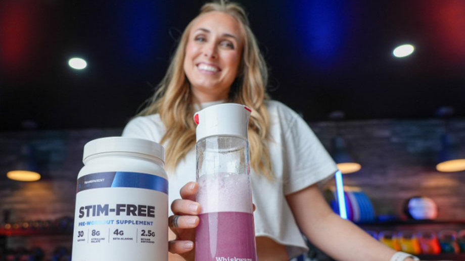 A woman holding a clear shaker bottle with a pink liquid in it next to a Transparent Labs stim-free pre-workout container