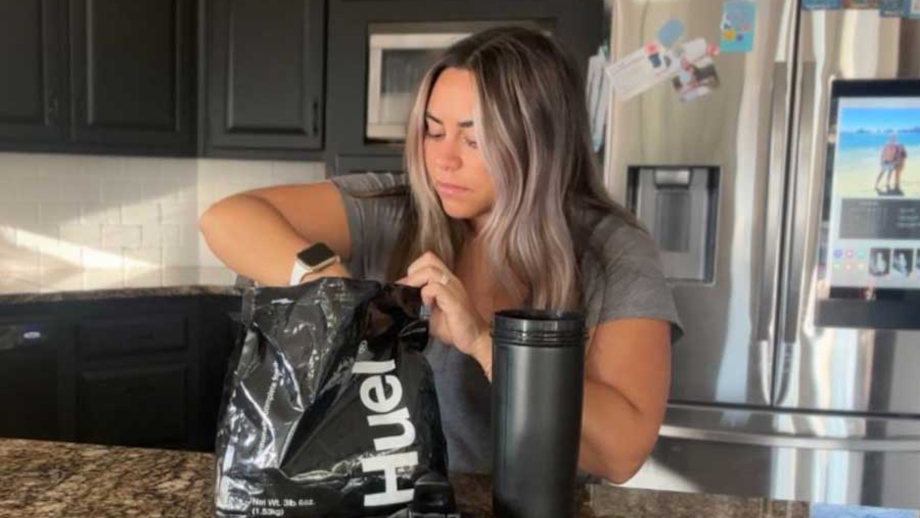 Woman scooping Huel Black out of bag into a shaker bottle