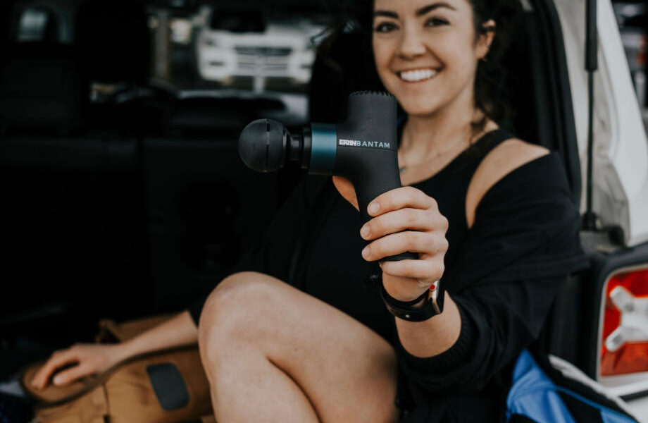 A smiling woman holds up an Ekrin Bantam mini massage gun