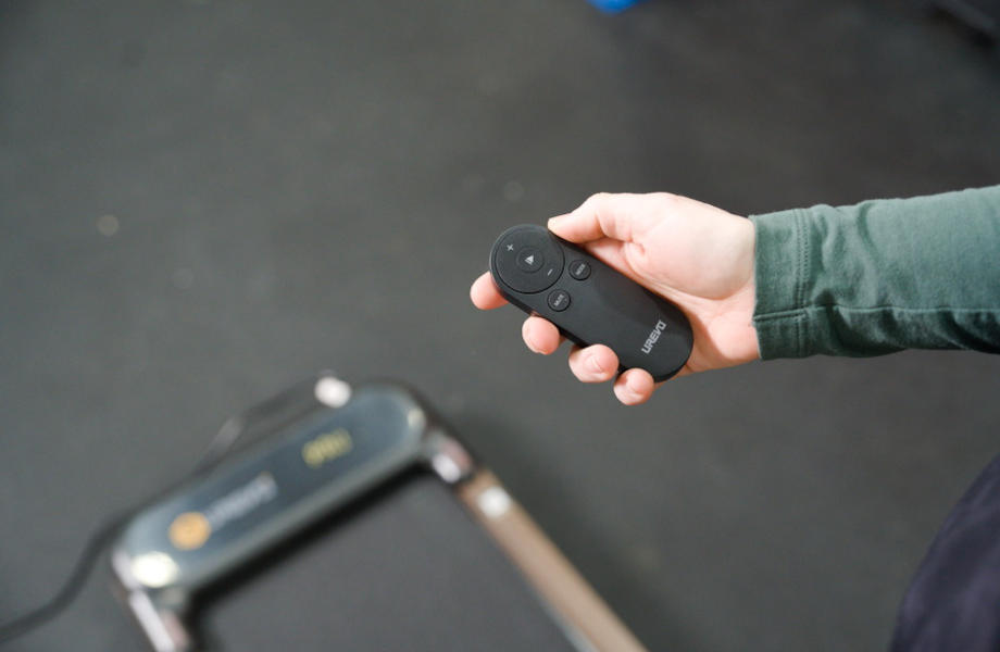 A person holds the remote control for a UREVO SpeceWalk E4W Treadmill.