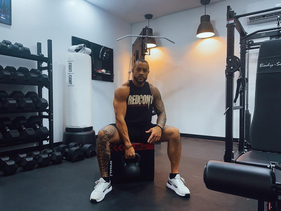 Stephen Sheehan, CPT, CNC, sits on a plyo box in a gym holding a Giant v3 24kg Kettlebell