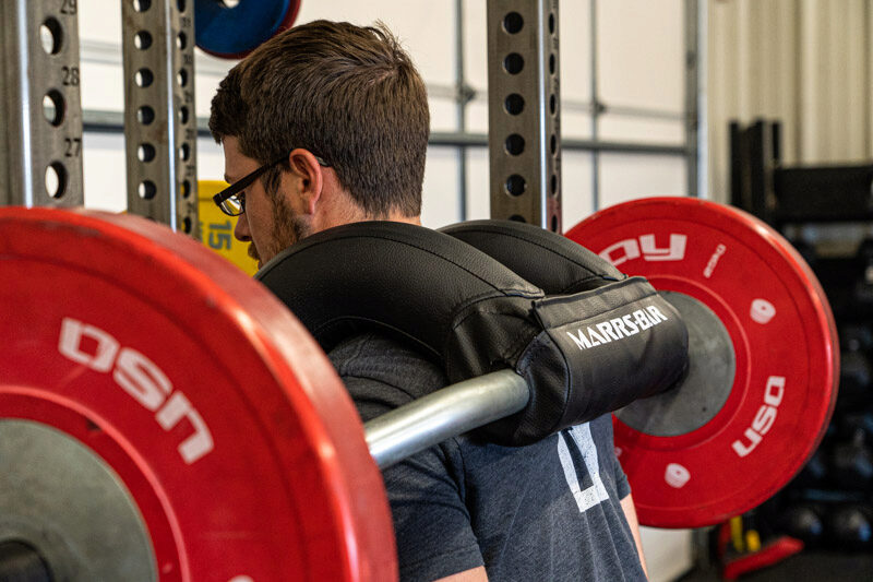 Man squatting with the Marrs-Bar with two red 45-pound weight plates