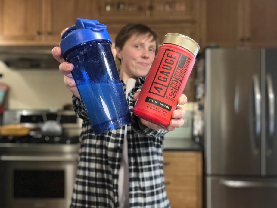 Woman holding up a shaker bottle and a canister of 4-Guage Pre-Workout that looks like a giant shotgun shell