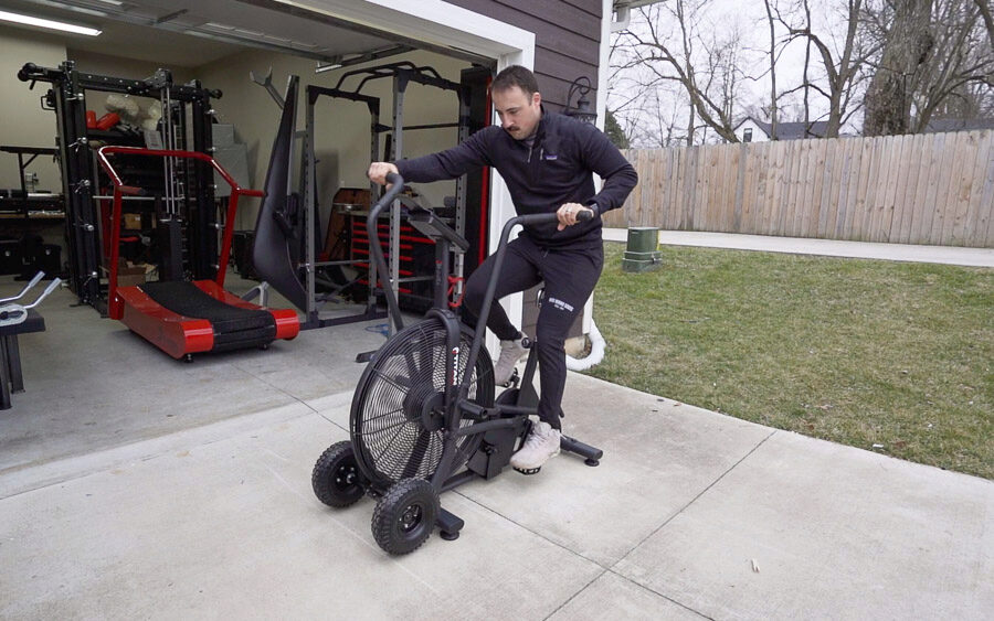 Coop is shown using his Titan Fan Bike outside of his garage gym.