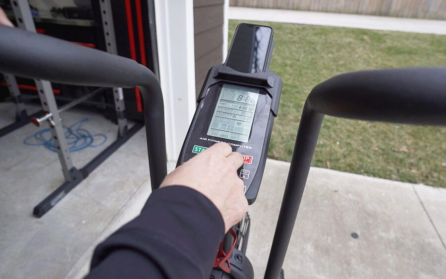 Coop pressing buttons on the LCD screen of the Titan Fitness Fan Bike.