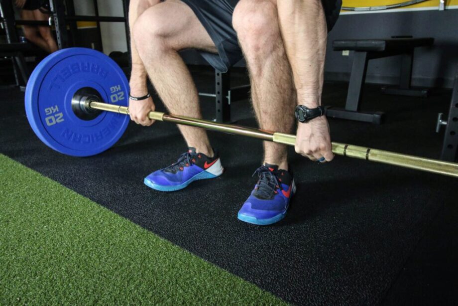 Man holding the bottom of a deadlift position with hands on a barbell