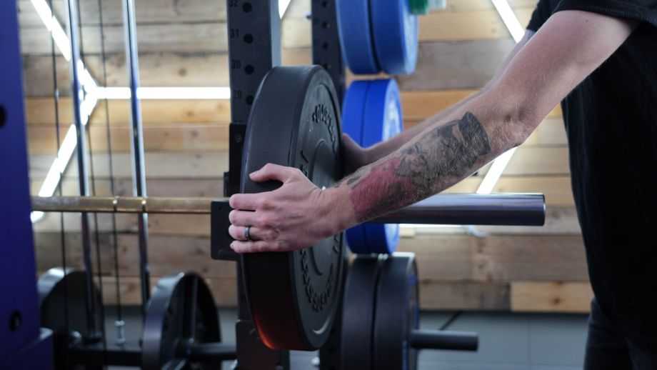 Loading Bells of Steel matte black bumper plate on barbell