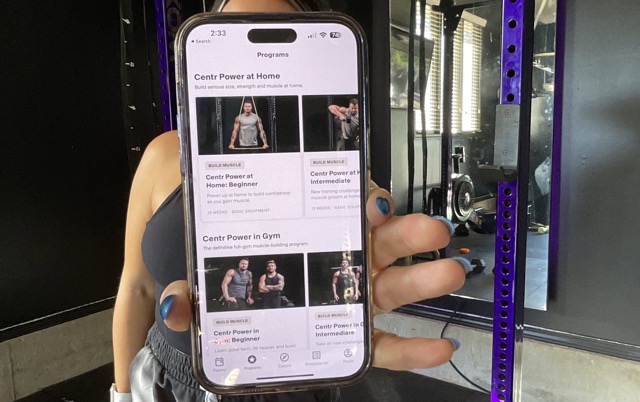 A woman in a gym holds her phone up to show the Centr app
