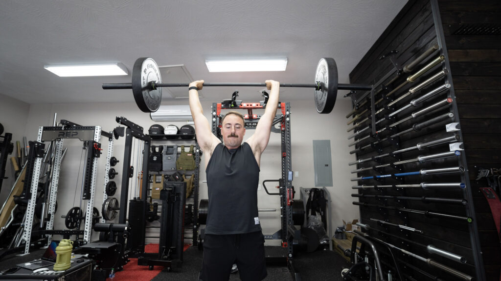 Man pressing a barbell with a 45-pound weight plate on each side overhead in a demonstration of one of the best barbell exercises.