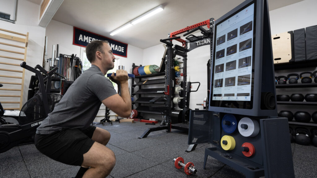 Coop squatting in front of the Tempo Studio during a smart home gym workout in his garage gym.