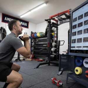 Coop squatting in front of the Tempo Studio during a smart home gym workout in his garage gym.