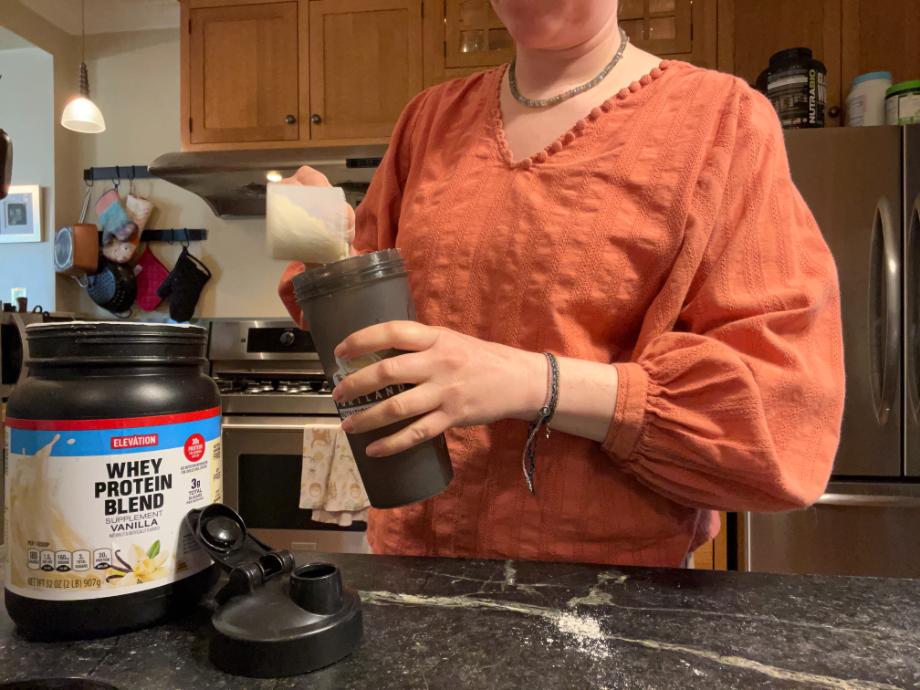 Woman scooping Elevation protein into a shaker cup