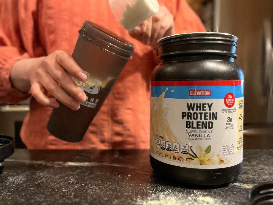 Woman scooping Elevation protein into a shaker cup