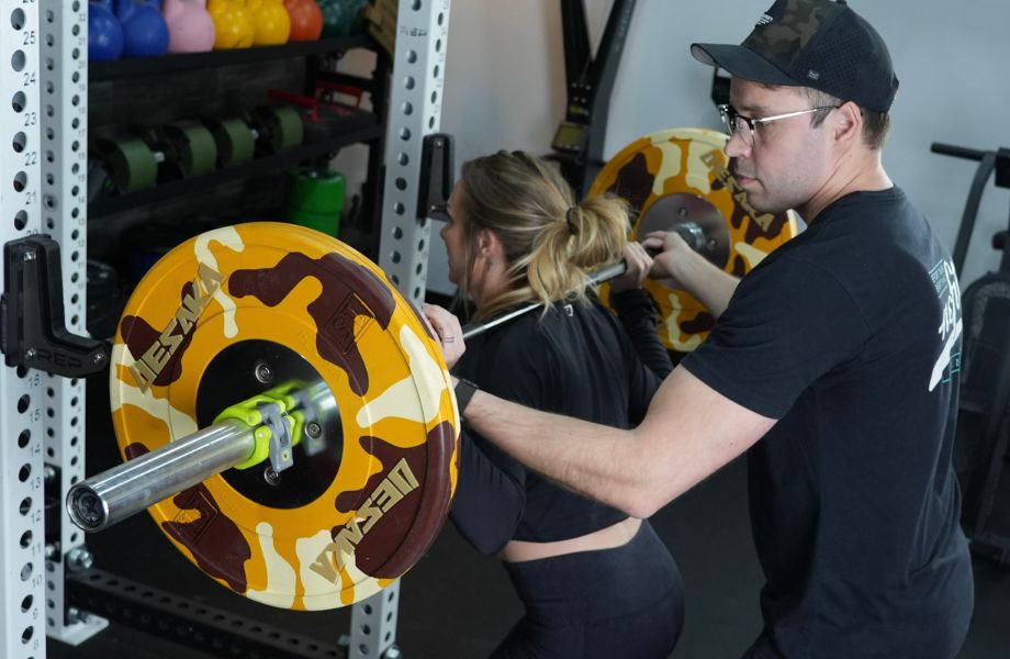 Personal trainer spotting female on squat