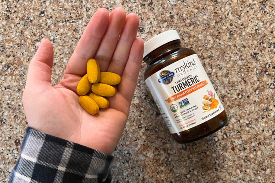 A hand holding Garden of Life brand organic turmeric tablets next to the supplement bottle