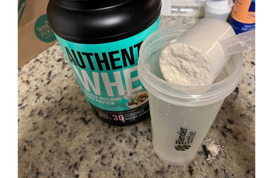 A scoop of Jacked Factory Whey being dumped into a clear Blender Bottle
