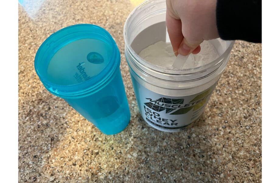 hand holding scoop over powder in bottle muscletech