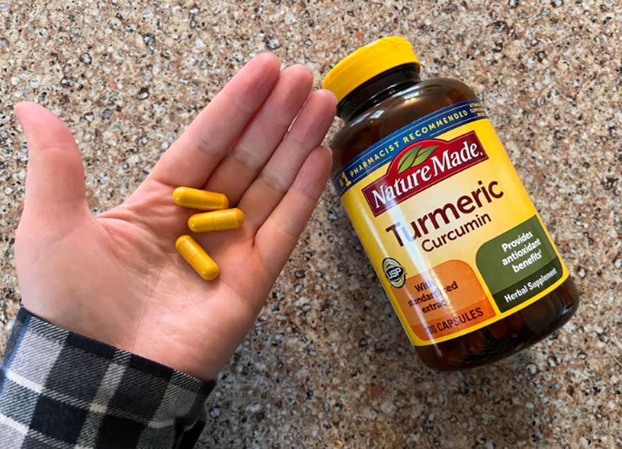 A hand holding three Nature Made Turmeric pills next to the supplement bottle