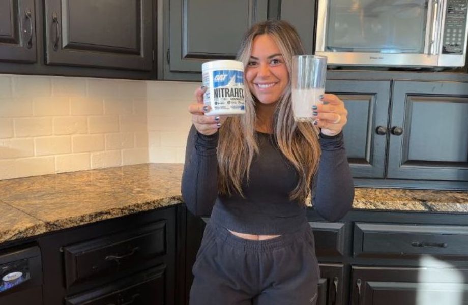 Woman holds up glass  and container of Nitraflex Pre-Workout