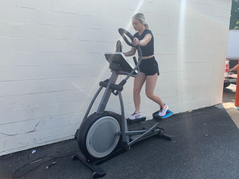 Full body shot of Caroline using the NordicTrack Commercial 14.9 elliptical. She is wearing all black clothing and pink Nike shoes.