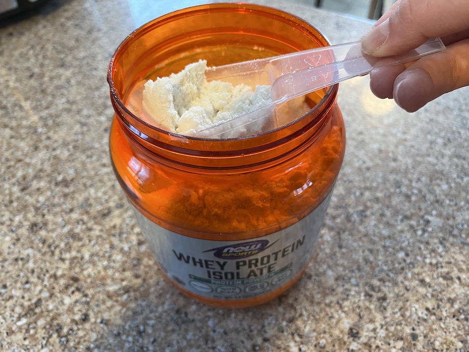 A hand scooping NOW sports whey protein isolate out of the container