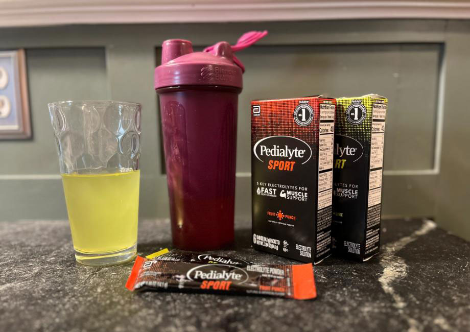 Some containers of Pedialyte Sport are next to a shaker cup and glass of liquid.