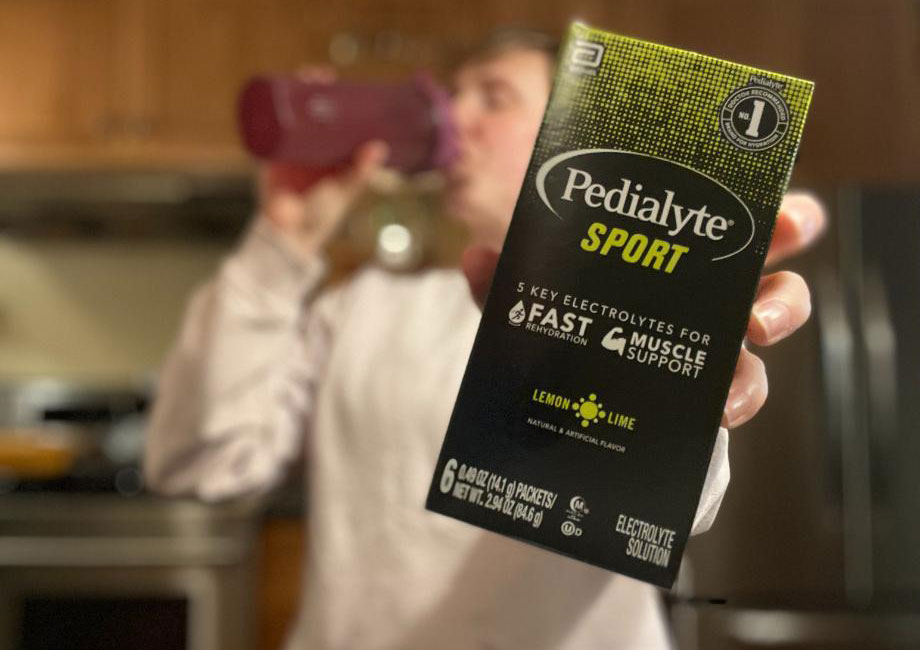Woman drinks from shaker while holding up a carton of Pedialyte Sport.