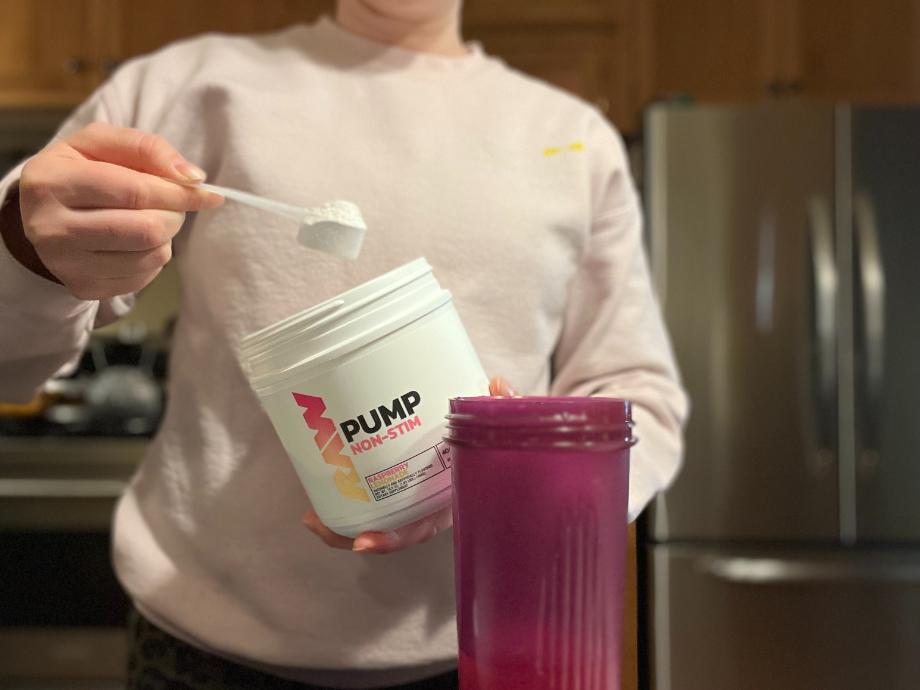 A woman scoops RAW Nutrition Pump pre-workout into a shaker.