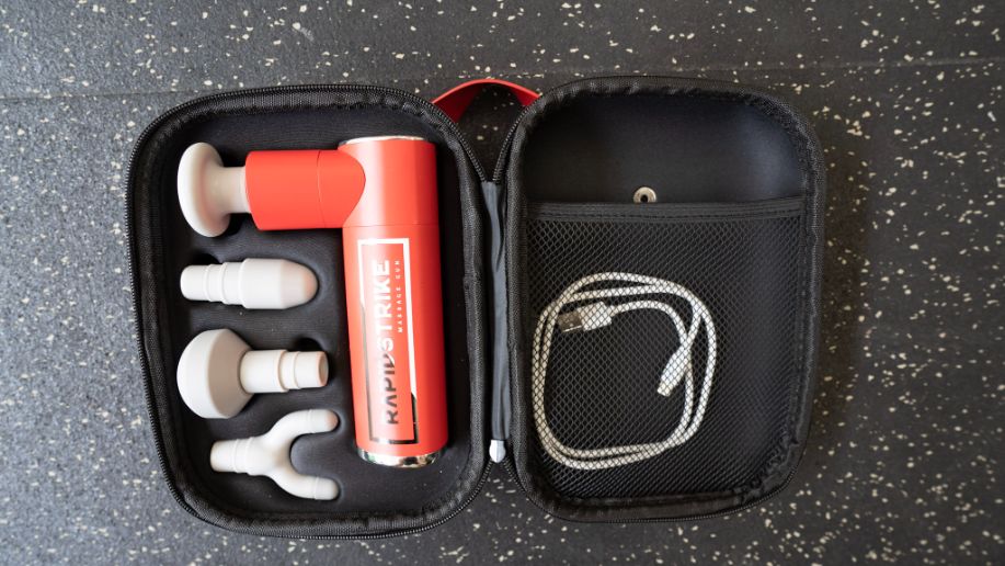 An aerial view of the REP Rapidstrike massage gun in its carrying case with attachments and charging cable.
