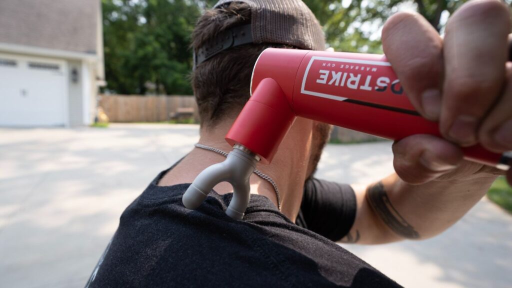 A man outdoors using the REP Rapidstrike massage gun with the fork attachment on his shoulder.