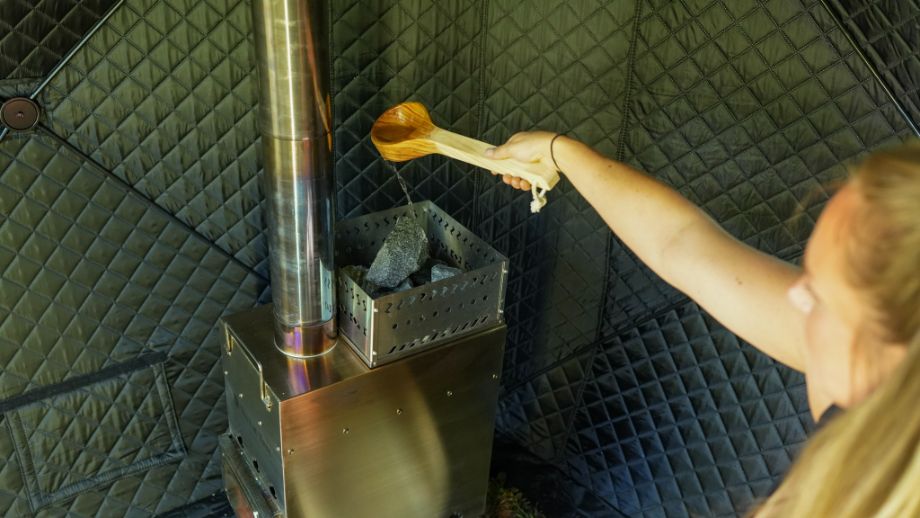 Woman ladling water on the hot sauna rocks inside SweatTent