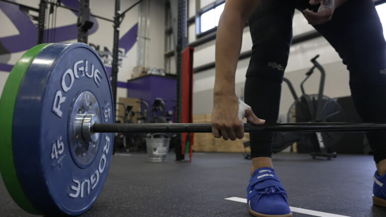 Woman wearing weightlifting shoes setting up for a barbell deadlift in a CrossFit gym.
