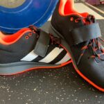 Pair of Adidas Adipower 2 weightlifting shoes near a blue bumper plate