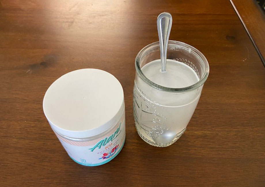 A mixed glass of Alani Nu BCAAs sits freshly stirred next to the canister.