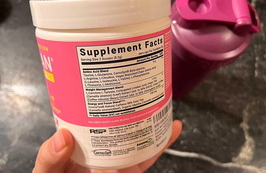 A hand holds a container of AminoLean Pre-Workout to display the Supplement Facts label