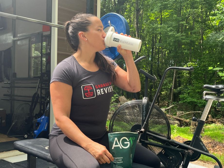 A woman drinking Athletic Greens AG1 out of a shaker cup