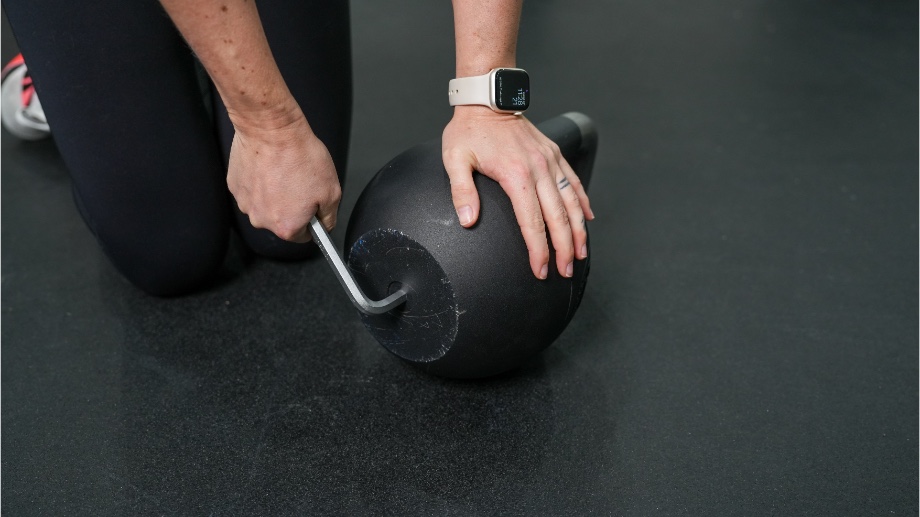 A close look at someone unscrewing the bottom of a Bells of Steel Adjustable Kettlebell.