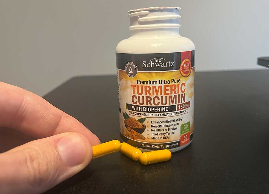 A hand holding a Bio Schwartz turmeric pill next to the supplement bottle