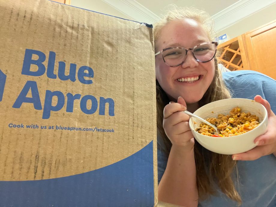 Blue Apron review cover image showing girl eating a meal by a Blue Apron box